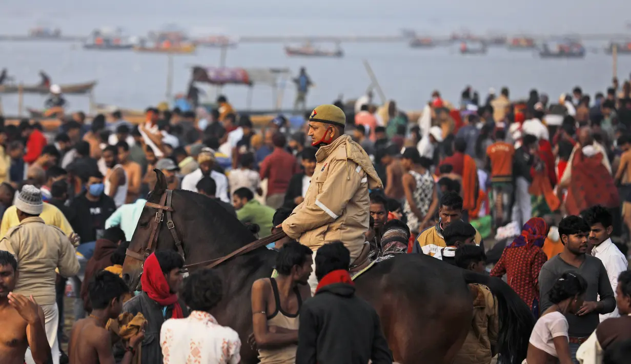 Seorang polisi, maskernya tergantung di dagu, berpatroli saat umat Hindu memadati pertemuan sungai Gangga dan Yamuna untuk ritual mandi pada festival Makar Sankranti di Prayagraj, India, 14 Januari 2022. Di India, orang yang tertangkap tanpa memakai masker akan didenda. (AP Photo/Rajesh Kumar Singh)