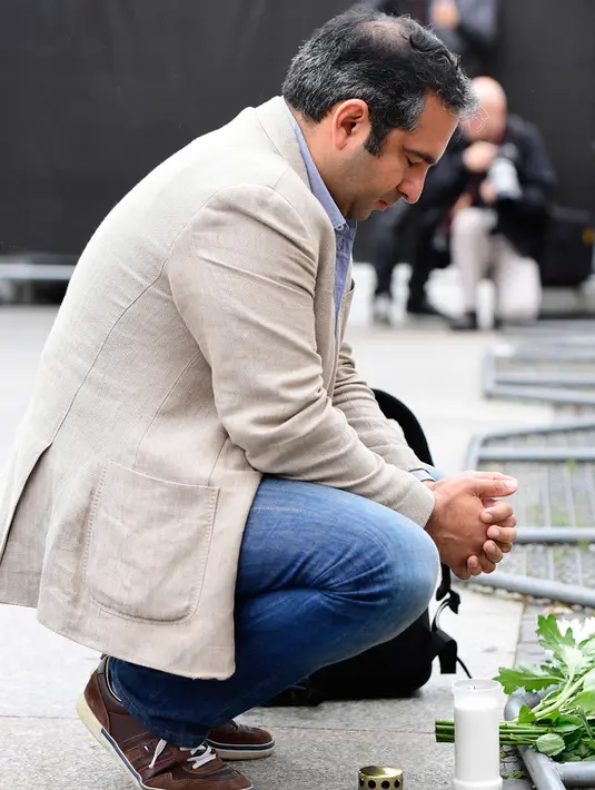 Seorang pria berdoa di samping lilin dan bunga di depan Kedutaan Besar Prancis di Berlin, Jerman (15/7). Karangan bunga tersebut untuk menghormati para korban teror Truk Maut saat perayaan hari Bastille di Nice. (AFP PHOTO/John MacDougall)