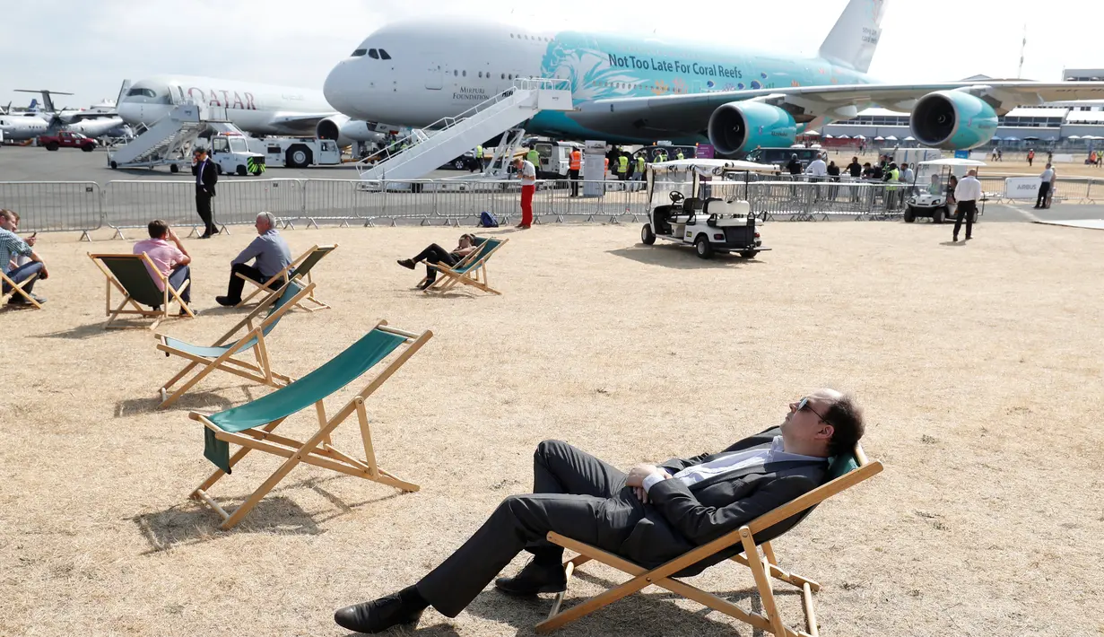 Pengunjung beristirahat di dek kursi dekat pesawat penumpang Airbus A380 di Farnborough Airshow, London, Inggris, Kamis (19/7). (Adrian DENNIS/AFP)