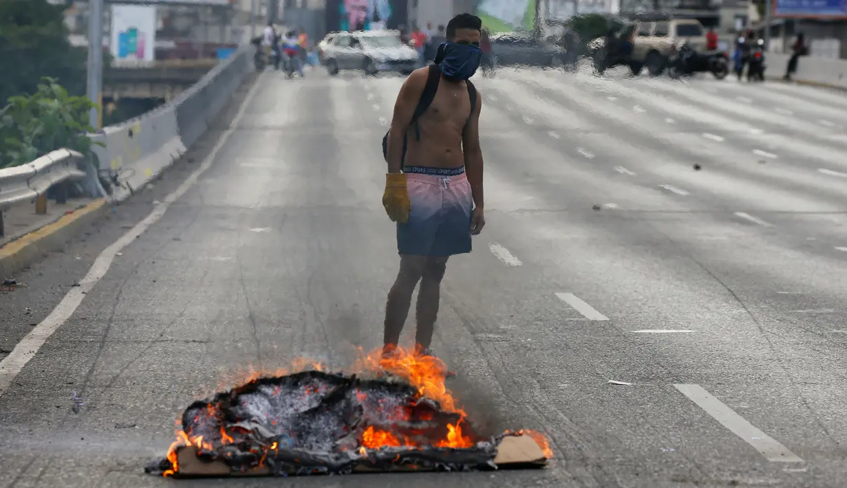 Seorang demonstran berdiri dekat kobaran api saat demonstrasi menuntut pengunduran diri Presiden Nicolas Maduro di Caracas, Venezuela, Sabtu (2/2). (AP Photo/ Fernando Llano)