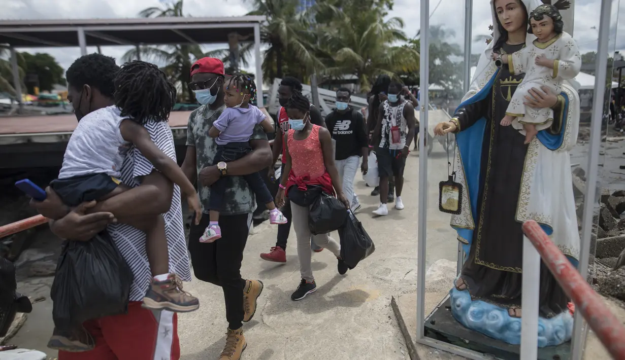 Para Migran Haiti berjalan menaiki perahu di Necocli, Kolombia, Rabu (28/7/2021). Ribuan migran terdampar di kota pelabuhan Kolombia saat mereka menunggu kapal menyeberang ke negara tetangga Panama dalam perjalanan mereka ke Amerika Serikat. (AP Photo/Ivan Valencia)