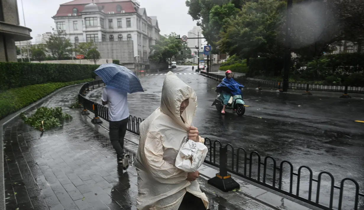 Pejalan kaki dan seorang pengendara sepeda motor menggunakan perlengkapan hujan saat cuaca buruk akibat Topan Bebinca di Shanghai pada Senin 16 September 2024. (Hector RETAMAL/AFP)