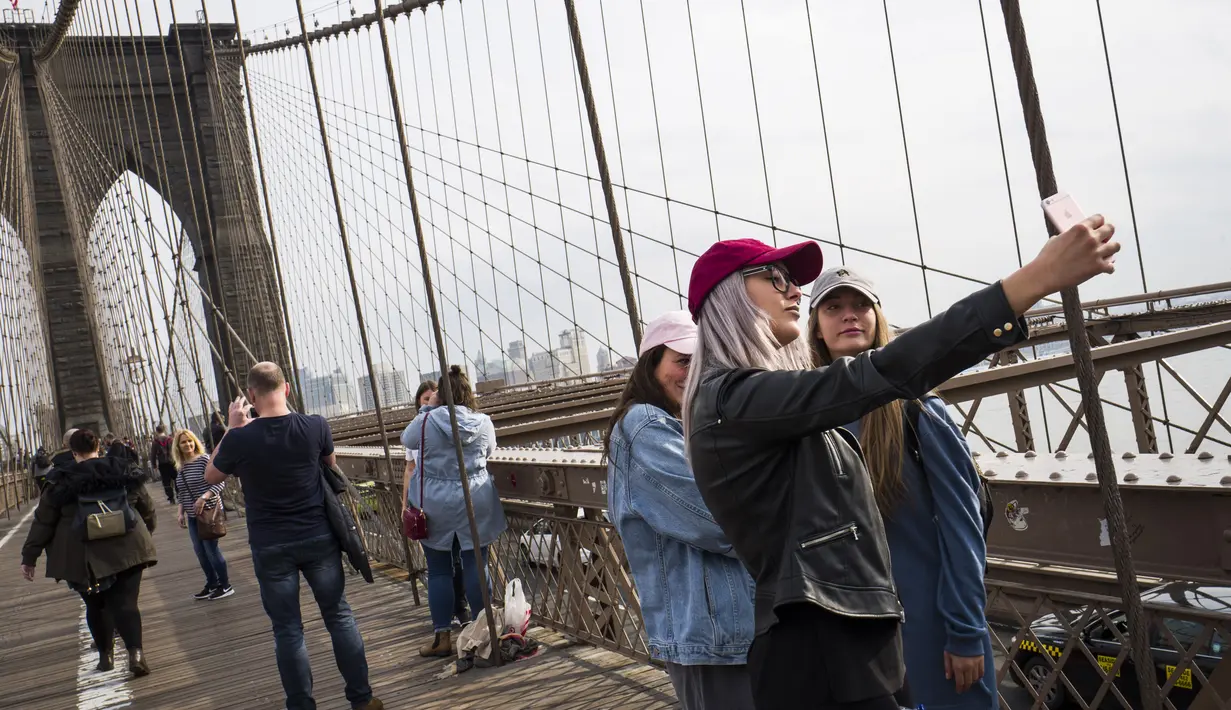 Turis mengambil foto di Jembatan Brooklyn, AS, Rabu (1/3). Menurut NYC & Co, larangan perjalanan yang sempat diucapkan Presiden Donald Trump telah menghambat minat pariwisata internasional. (Drew Angerer / Getty Images / AFP)