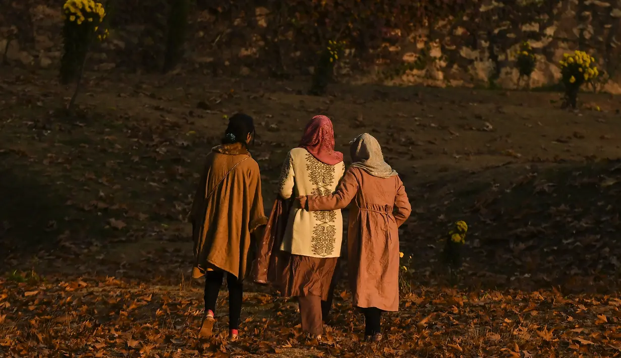 Para wanita berjalan melewati pepohonan yang merontokkan daun musim gugur mereka di taman Nishat Bagh di Srinagar (16/11/2020). (AFP/Tauseef Mustafa)