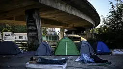 Seorang pencari suaka asal Afghanistan tidur di luar kamp darurat di sebuah kamp migran darurat yang terletak di bawah jembatan jalan raya A1 di utara pinggiran Kota Paris Saint-Denis di Prancis (16/9/2020). (AFP/Christophe Archambault)