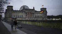 Orang-orang berjalan di depan Gedung Reichstag dan Bundestag di Berlin, Jerman, 17 November 2021. Badan pengendalian penyakit Jerman melaporkan 52.826 kasus baru COVID-19 pada 17 November 2021 karena tingkat infeksi terus meningkat. (AP Photo/Markus Schreiber)