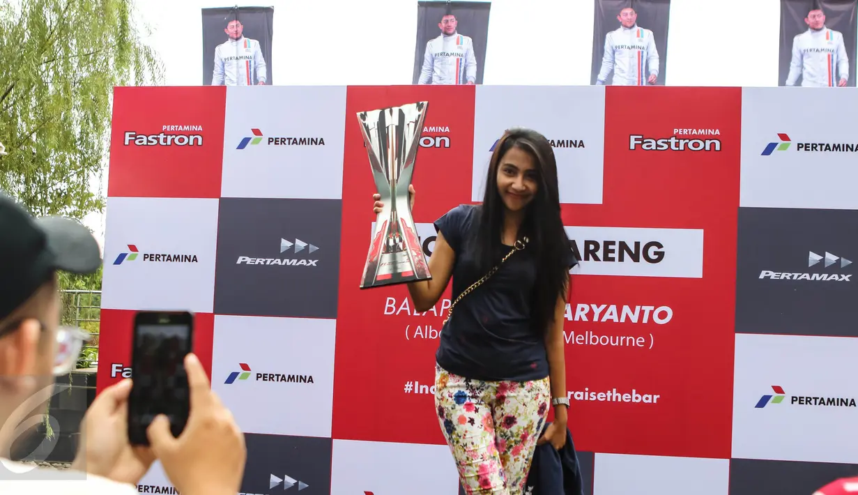Seorang pengunjung berpose dengan piala F1 di arena acara Nonton Bareng F1 GP Australia 2016 Pertamina di Mall Bintaro Xchange, Tangerang Selatan, Minggu (20/3). Acara tersebut terbuka untuk umum, termasuk fans Rio Haryanto. (Liputan6.com/Fery Pradolo)
