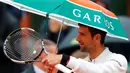 Petenis Serbia, Novak Djokovic, memakai payung saat memasuki lapangan jelang melawan petenis Spanyol, Roberto Bautista Agut, dalam laga Prancis Terbuka 2016 di Roland Garros, Prancis, (31/5/2016). (Reuters/Gonzalo Fuentes)