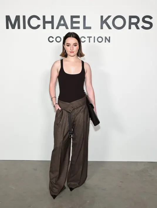 <p>Kaitlyn Dever mengenakan chocolate viscose bodysuit dengan glen plaid wool slouch trousers, menciptakan harmoni antara maskulin dan feminin. [Dok/Michael Kors].</p>