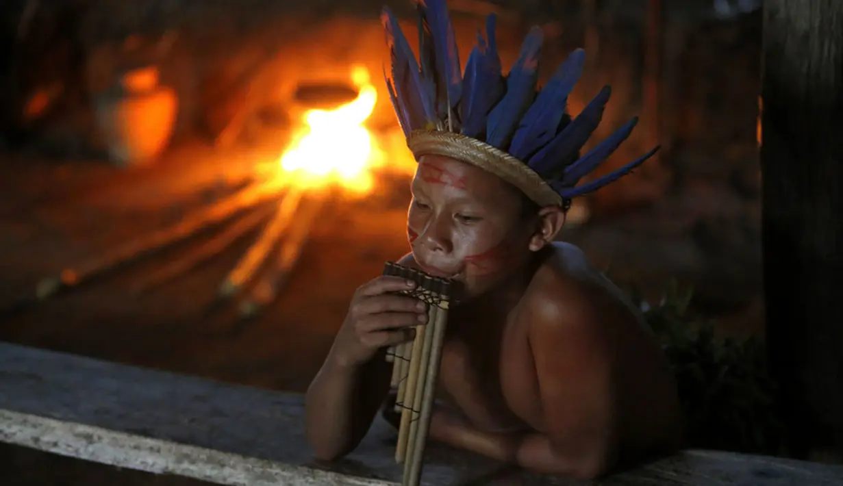 Salah satu warga suku Amazon Tatuyo terlihat memainkan musik tradisional di desanya, Rio Negro (Black River) dekat salah satu kota penyelenggara pertandingan Piala Dunia 2014, Manaus City, Brasil  (23/6/2014). (REUTERS/Andres Stapff)