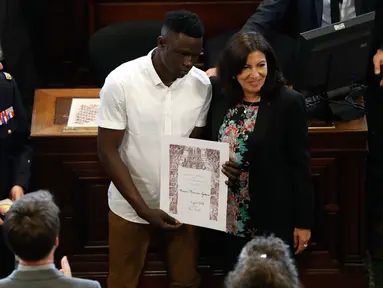 Imigran Mali Mamoudou Gassama dianugerahi medali Grand Vermeil oleh walikota Paris Anne Hidalgo (kanan) di Paris, Prancis (4/6). Sebelumnya Mamoudou dijuluki "Spider-Man" karena menyelamatkan balita yang nyaris jatuh dari apartemen. (AFP/Francois Guillot)