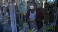 Warga tercermin di panel pintu saat mengantre untuk membeli obat di apotek di Beijing, Selasa (13/12/2022). Beberapa universitas di China mengatakan akan mengizinkan mahasiswanya menyelesaikan semester dari rumah dengan harapan mengurangi potensi wabah COVID-19 yang lebih besar selama kesibukan perjalanan Tahun Baru Imlek di bulan Januari mendatang. (AP Photo/Andy Wong)