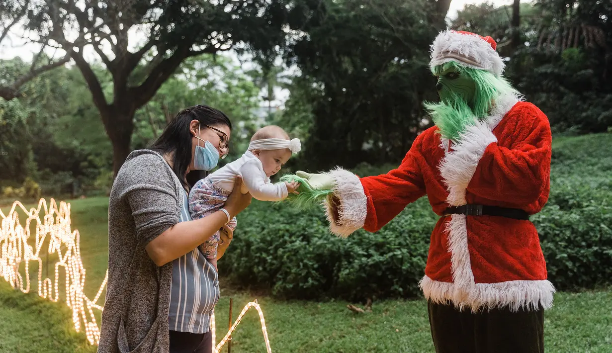 <p>Alexi Wright, 6 bulan (tengah) menjangkau Grinch berpakaian sebagai Santa Claus sementara ibunya, Kerrin (kiri), melihat selama kunjungan ke "Trail of Lights" Kebun Raya Durban menjelang Natal di Durban, Afrika Selatan (14/12/2021). (AFP/Rajesh Jayantilal)</p>