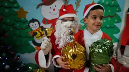 Seorang anak laki-laki Palestina sambil membawa kado foto bersama dengan santa claus  saat perayaan menyambut Hari Natal di Sekolah Amerika di Kota Gaza (20/12).  (AFP Photo/Mohammed Abed)