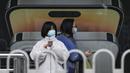 Seorang wanita yang mengenakan masker berjalan dengan yang lain menggunakan iPhone saat mereka menunggu bus mereka di halte bus yang menampilkan iklan iPhone di Beijing pada Minggu (30/10/2022). Para pekerja iPhone Apple Inc meninggalkan pabrik karena lokasinya berada dalam zona industri Kota Zhengzhou yang sedang diberlakukan lockdown setelah adanya 64 laporan kasus virus corona di kawasan tersebut. (AP Photo/Andy Wong)