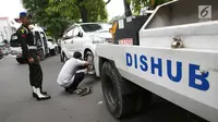 Petugas Dinas Perhubungan mengaitkan kendaraan pada mobil derek di kawasan Pasar Baru, Jakarta, Kamis (14/12). Parkir sembarang di pinggir jalan ini membuat kesemrawutan dan menimbulkan kemacetan. (Liputan6.com/Immanuel Antonius)