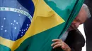 Mantan presiden Brasil (2003-2010) dan kandidat presiden dari Partai Pekerja (PT) berhaluan kiri, Luiz Inacio Lula da Silva, muncul di belakang bendera nasional Brasil selama kampanye di Sao Mateus, Negara Bagian Sao Paulo, Brasil, Senin (17/10/2022). Lula da Silva dan presiden Jair Bolsonaro akan menghadapi putaran kedua pemilihan presiden pada 30 Oktober, dengan ekspektasi persaingan ketat mendorong kedua belah pihak untuk mengintensifkan kampanye pemilihan. (Miguel SCHINCARIOL / AFP)