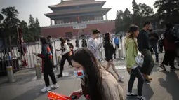 Seorang wanita mengenakan masker untuk mencegah penyebaran virus corona memegang bendera nasional Kota Terlarang selama Hari Nasional di Beijing, Rabu, (7/10/2020). Turis Tiongkok melakukan 425 juta perjalanan domestik pada paruh pertama dari delapan hari libur Hari Nasional. (AP Photo/Andy Wong)