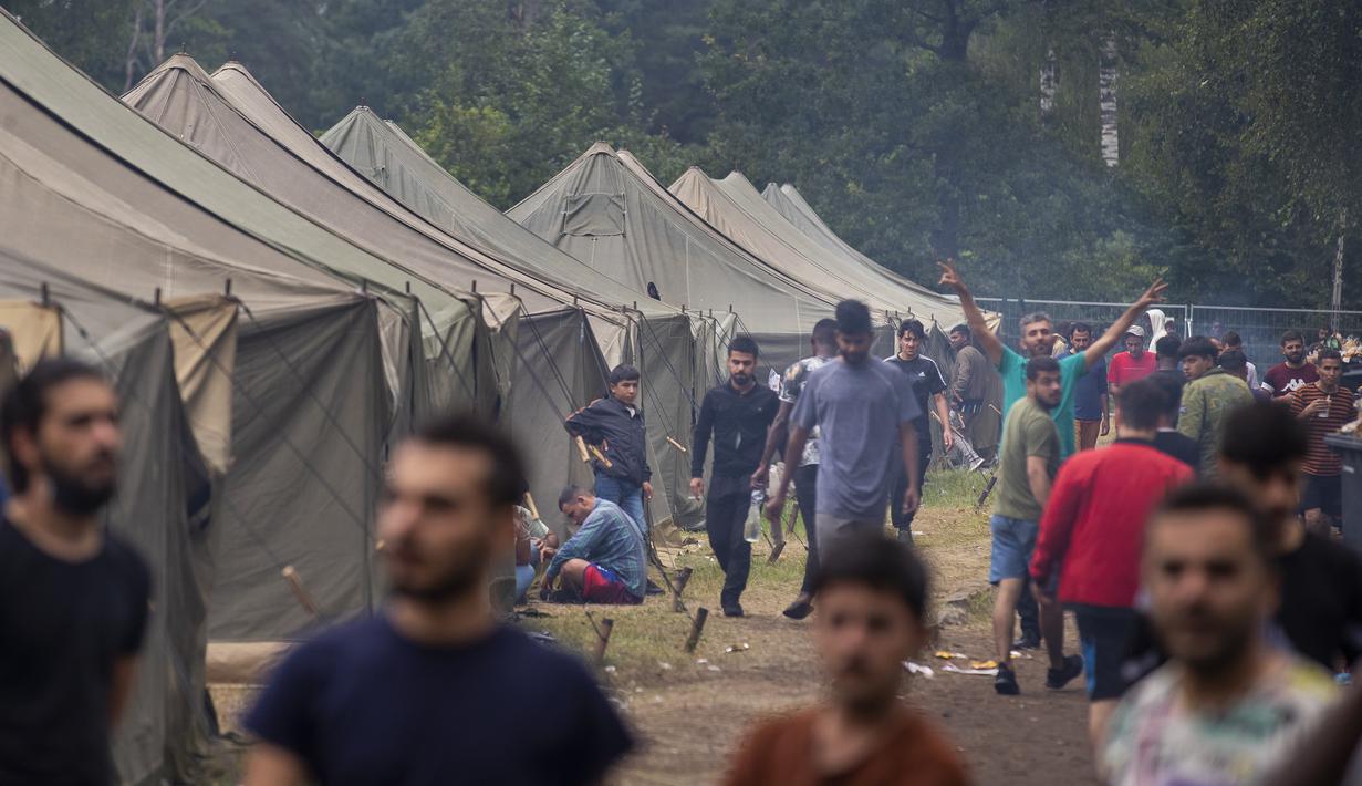 Para migran berjalan di dalam kamp pengungsi yang baru dibangun di tempat latihan militer Rudninkai, sekitar 38km (23,6 mil) selatan dari Vilnius, Lituania, Rabu (4/8/2021). (AP Photo/Mindaugas Kulbis)
