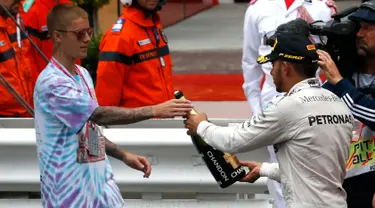 Pembalap Mercedes F1 Lewis Hamilton memberikan sampanye kepada penyanyi Justin Bieber usai berhasil menjuarai Grand Prix di Monaco, (29/5). Hamilton menjadi yang tercepat dengan mencatatkan waktu satu jam 59 menit 29,133 detik. (REUTERS/Eric Gaillard)