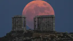 Bulan Purnama Stroberi atau Strawberry Full Moon muncul di belakang Kuil Poseidon marmer kuno di Cape Sounion, sekitar 70 Km selatan kota Athena, Yunani, Kamis (24/6/2021). Julukan ini disematkan oleh suku asli Amerika yang dipopulerkan dalam Farmers Almanac. (AP Photo/Petros Giannakouris)
