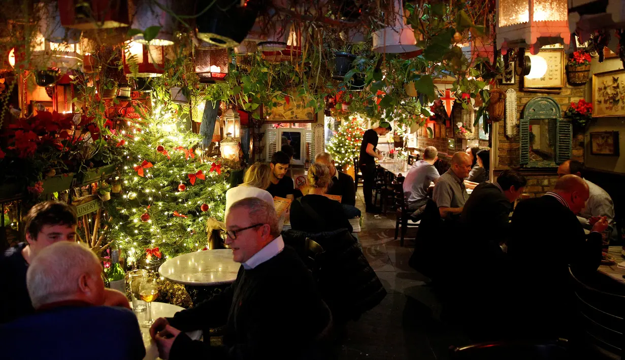 Pelanggan berbincang di bar The Churchill Arms dengan dekorasi Natal, London, Inggris, 20 Desember 2016. Menyambut Natal, bagian luar bangunan bar tersebut ditutupi lebih dari 80 pohon natal dan hampir 22.000 lampu berkelap-kelip. (REUTERS/Neil Hall)