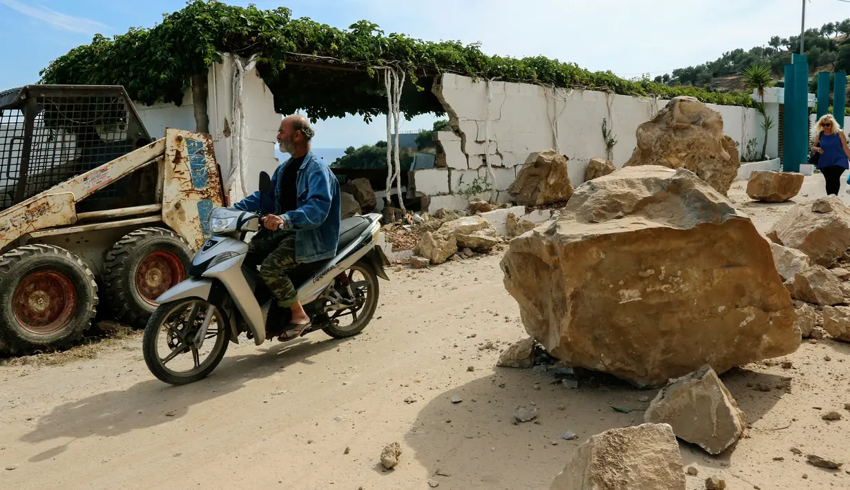 Pengendara sepeda motor melintasi puing-puing bangunan yang rusak akibat gempa bumi di Pulau Lesbos, Yunani Timur, Senin (12/6). Laporan televisi lokal menyebut jalan utama menuju pusat kota di pulau itu rusak akibat tanah longsor. (STRINGER / AFP)