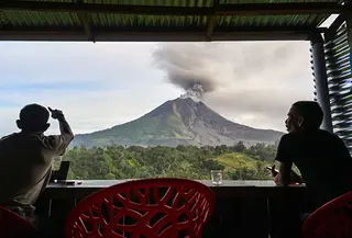 Dua pria menyaksikan Gunung Sinabung menyemburkan abu dan asap tebal dari wilayah Karo, Provinsi Sumatra Utara, Rabu, 2 September 2026. (AFP/ YT Haryono)
