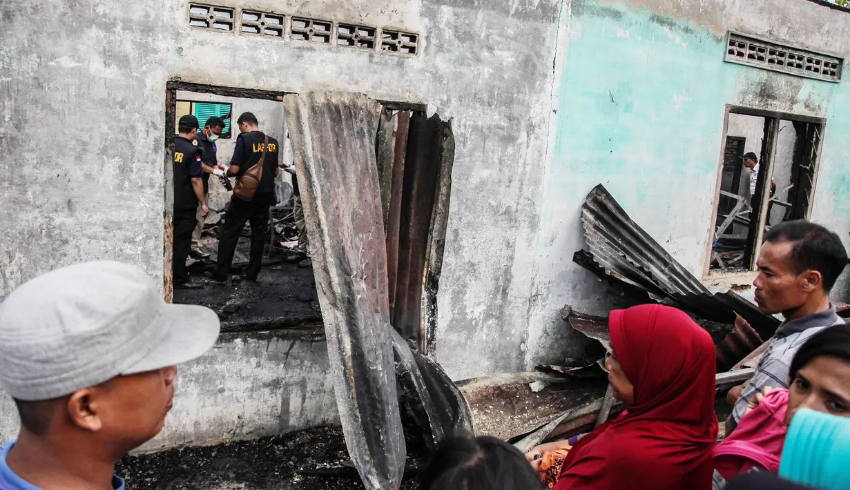 Warga menyaksikan tim penyelidik bekerja di lokasi kebakaran pabrik korek gas di Binjai, Langkat, Sumatera Utara, (21/6/2019). Pihak kepolisian masih melakukan penelusuran, terutama jenazah korban. (Ivan Damanik/AFP)