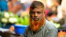 Dalam gambar yang diambil pada 24 Desember 2018, penjual sayur bernama Munir Hossain berpose dengan janggut oranye di Dhaka. Ternyata bukan hanya janggut saja yang mereka warnai, bagian rambut di kepala juga diwarnai dengan henna dan karena banyak yang menggunakannya. (MUNIR UZ ZAMAN / AFP)