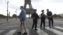 Seorang turis Rusia memegang sebotol sampanye berjalan melewati petugas polisi yang mengamankan jembatan menuju Menara Eiffel di Paris, Rabu (23/9/2020). Polisi Paris telah memblokir daerah sekitar Menara Eiffel setelah ancaman bom telepon. (AP Photo / Michel Euler)