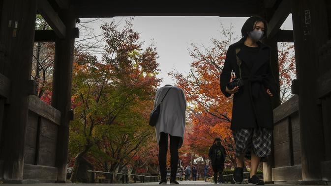 Seorang perempuan membungkuk sebelum keluar dari gerbang kuil Buddha Joshinji sementara pengunjung yang mengenakan masker mengamati warna dedaunan musim gugur yang jatuh di Tokyo, Jepang pada 9 Desember 2020. (AP Photo/Kiichiro Sato)