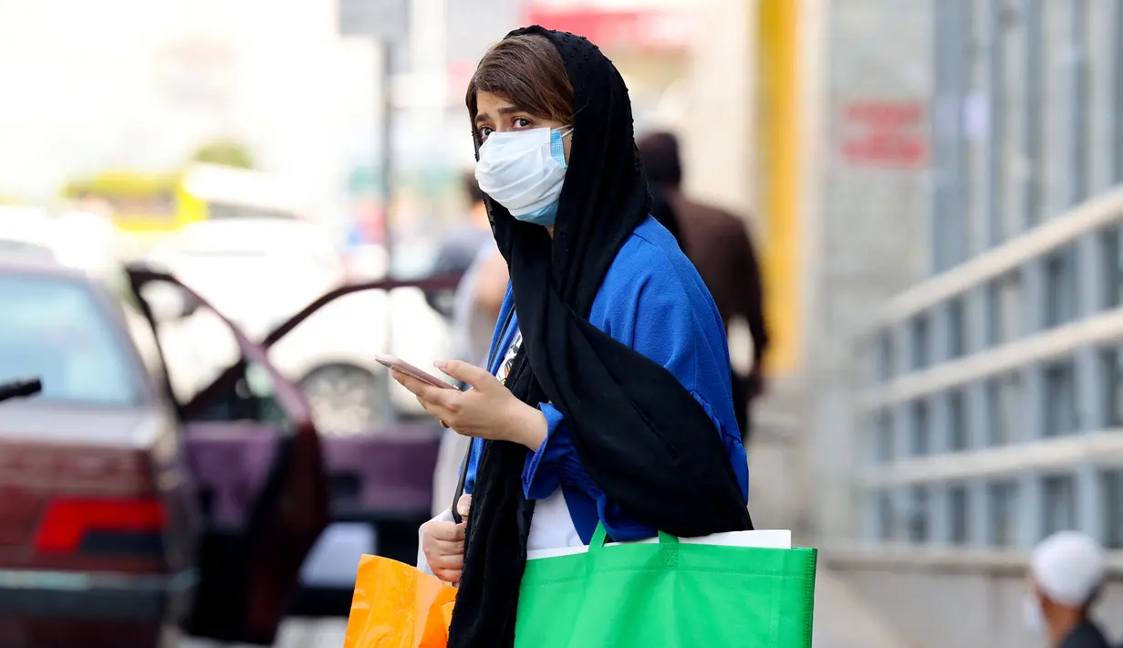 Seorang wanita Iran yang mengenakan masker menunggu untuk menyeberang jalan di ibu kota Teheran, Sabtu (3/7/2021). Presiden Hassan Rouhani mengaku khawatir Iran akan dilanda gelombang kelima pandemi Covid-19 karena kemunculan virus corona varian Delta. (ATTA KENARE/AFP)