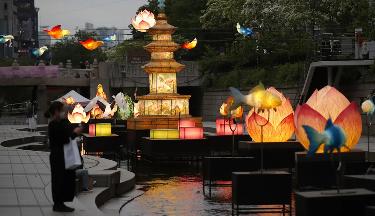 Pengunjung yang mengenakan masker wajah sebagai tindakan pencegahan penyebaran virus corona COVID-19 berjalan dekat lentera yang dipajang untuk perayaan ulang tahun Buddha pada 19 Mei mendatang di Seoul, Korea Selatan, Senin (10/5/2021). (AP Photo/Lee Jin-man)