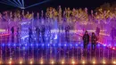 Orang-orang berdiri di dalam pertunjukan cahaya Natal dan tampilan air mancur yang disinkronkan di Experience Park, di distrik pesisir Hellenikon, Athena, Senin (20/12/2021). (AP Photo/Petros Giannakouris)