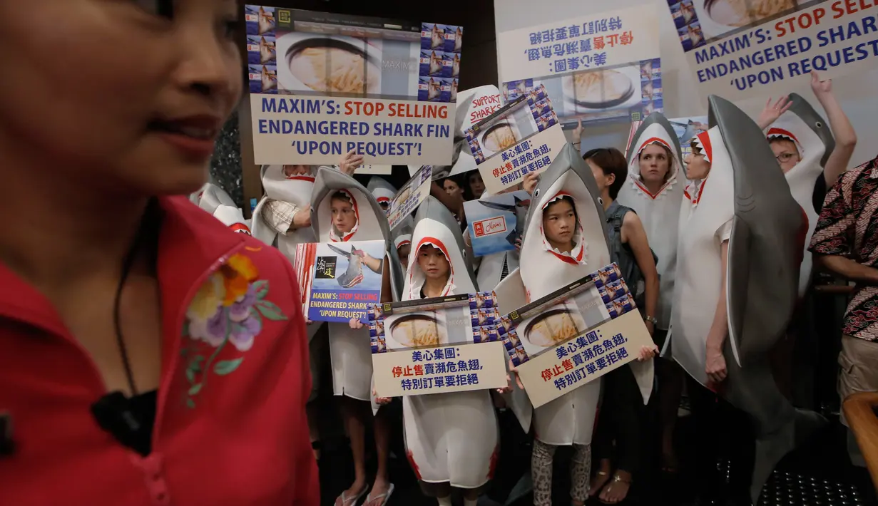 Pekerja restoran China (kiri) berdiri di samping sekelompok aktivis konservasi hewan yang mengenakan kostum hiu saat melakukan demonstrasi di depan restoran di Hong Kong (10/6). (AP Photo / Kin Cheung)