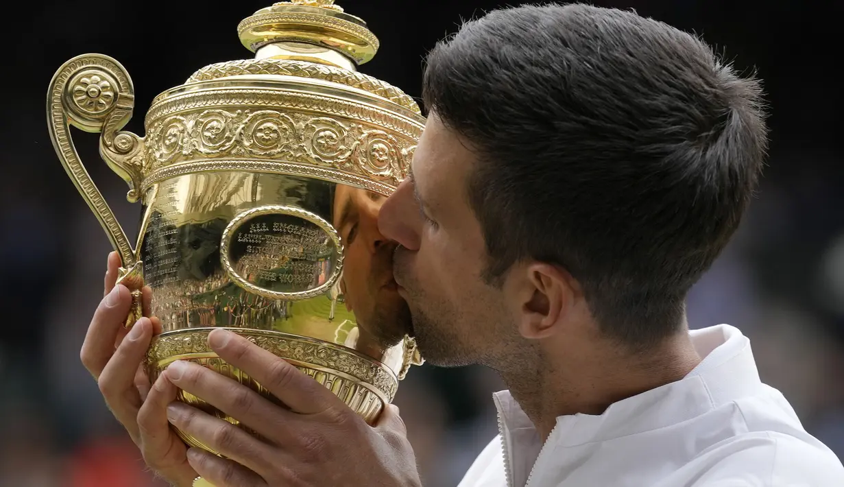 Petenis Serbia, Novak Djokovic cium Piala Wimbledon usai kalahkan petenis Italia, Matteo Berrettini di partai puncak tunggal putra. Kemenangan ini mengantarkan Djokovic menyamai rekor Nadal dan Federer sebagai petenis yang mampu mendapatkan 20 gelar Grand Slam. (Foto: AP/Kirsty Wigglesworth)