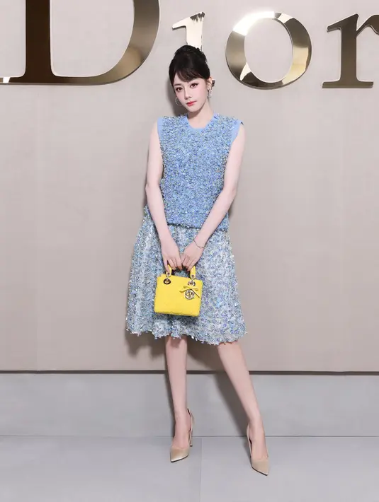 Dilraba Dilmurat tampil feminin dengan setelan sweater dan cotton skirt embroidery dari Dior. Bergaya ala Audrey Hepburn, ia jinjing tas Lady Dior kuning yang menyala [Dior]