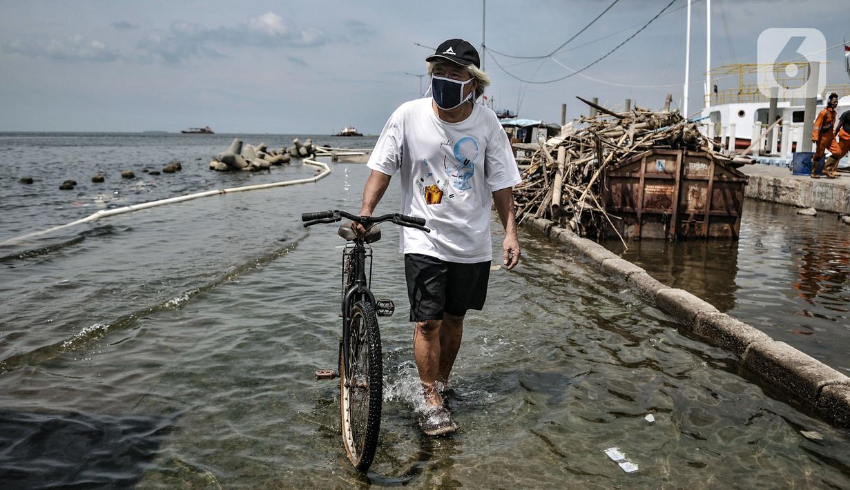Warga menuntun sepeda saat melintasi banjir rob di Pelabuhan Kali Adem, Muara Angke, Jakarta, Kamis (22/10/2020). Banjir akibat air pasang dengan ketinggian mencapai 30 cm tersebut telah merendam kawasan Pelabuhan Kali Adem dan sudah berlangsung selama lima hari. (merdeka.com/Iqbal S. Nugroho)