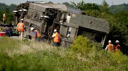 Pekerja memeriksa lokasi kereta Amtrak yang tergelincir setelah menabrak truk sampah di dekat Mendon, Missouri, AS (27/6/2022). Peristiwa itu terjadi sehari setelah kereta lain yang dioperasikan Amtrak bertabrakan dengan kendaraan penumpang di perlintasan kereta api di California, yang mengakibatkan tiga kematian. (AP Photo/Charlie Riedel)