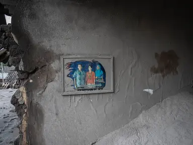 Sebuah potret keluarga masih tergantung di sebuah rumah yang rusak akibat erupsi Gunung Semeru di Desa Sumber Wuluh, Lumajang, Jawa Timur, Senin (6/12/2021). Desa Sumber Wuluh luluh lantak diterjang erupsi Semeru mengakibatkan puluhan rumah rusak dan ratusan warga mengungsi. (Juni Kriswanto/AFP)