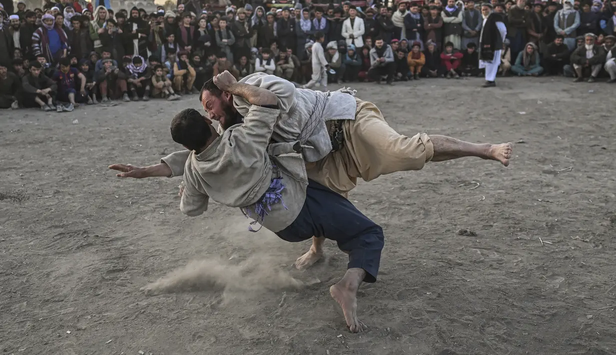 Pria Afghanistan bergulat di latar belakang selama tontonan gulat mingguan yang diadakan di arena darurat di taman Chaman-e-Hozori, di Kota Kabul (12/11/2021). (AFP/Hector Retamal)