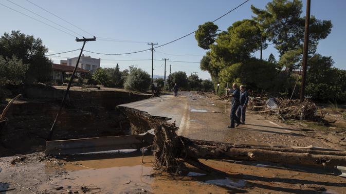 Warga memeriksa jalan yang rusak setelah badai di desa Kineta, Athena (25/11/2019). Ratusan rumah terendam banjir setelah badai semalam menerjang daerah barat Athena. (AP Photo/Petros Giannakouris)