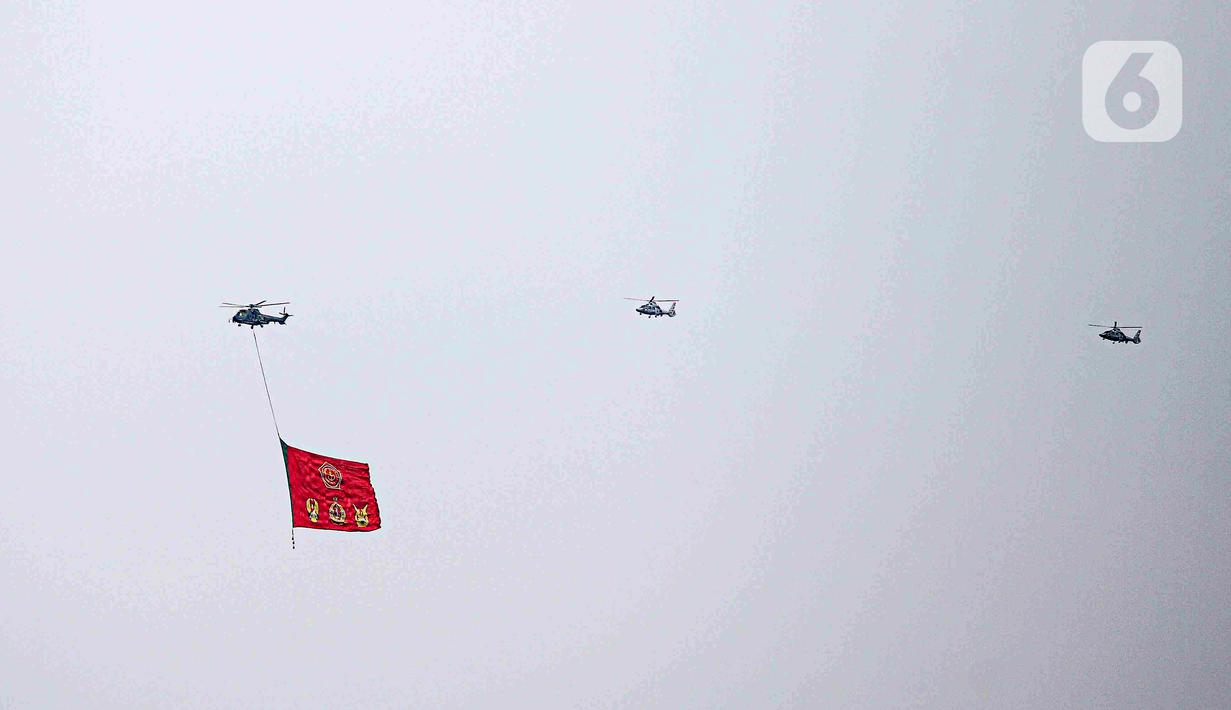 Helikopter TNI AU mengibarkan bendera Trimatra raksasa di kawasan Gedung DPR RI, Jakarta, Selasa (5/10/2021). TNI AU mengerahkan enam helikopter yang membawa bendera Merah Putih serta bendera Trimatra raksasa. (Liputan6.com/Faizal Fanani)