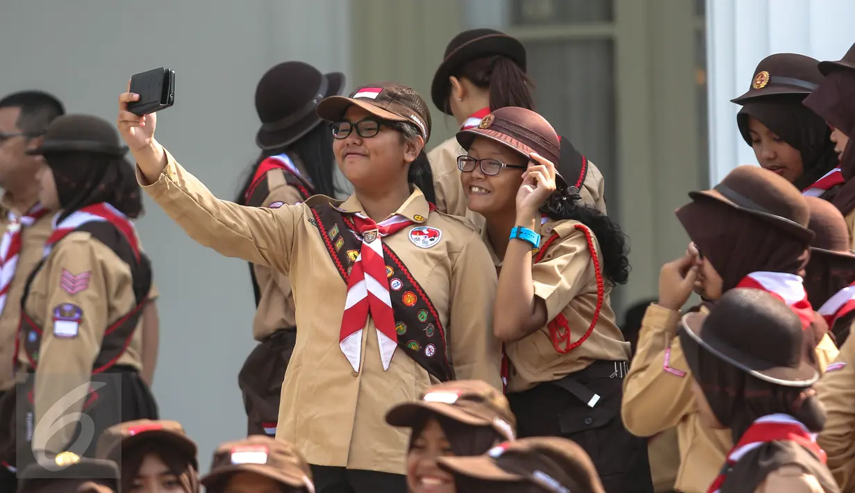 Seorang wanita dari delegasi gerakan Pramuka Indonesia tampak berselfie ria di Halaman Istana Merdeka, Jakarta, Jumat (24/7/2015). 462 kontingen Pramuka Indonesia yang akan mengikuti Jambore Pramuka Dunia ke-23. (Liputan6.com/Faizal Fanani)c