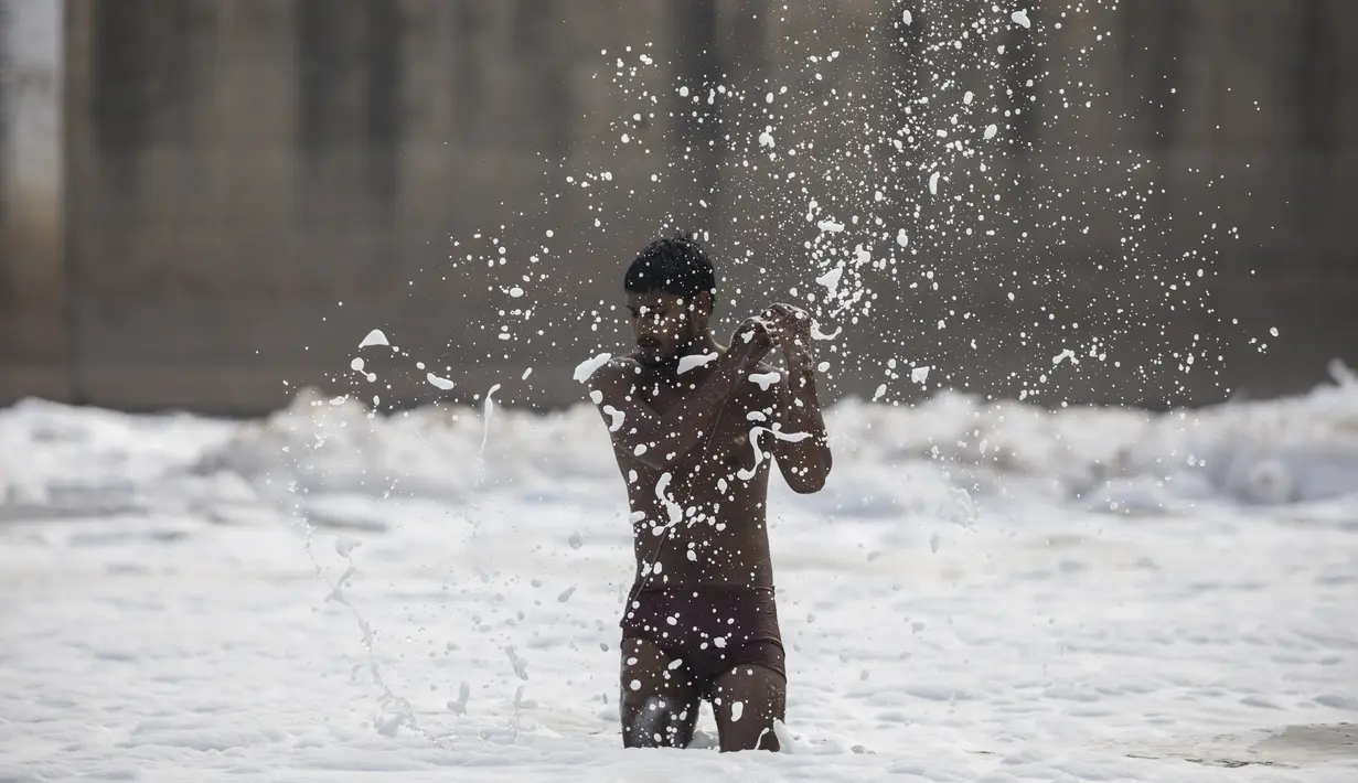 Seorang pemuda mencipratkan busa ketika mendingin di sungai Yamuna yang tercemar di pinggiran New Delhi (23/7/2020). Sungai ini menyandang gelar sebagai sungai paling tercemar di dunia. (AFP Photo/Xavier Galiana)