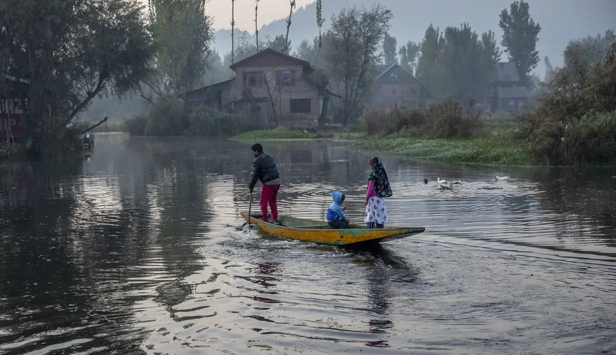 Seorang pria Kashmir bersama anak-anaknya mendayung perahunya di danau Dal di Srinagar, Kashmir yang dikuasai India (18/10/2020). (AP Photo/Dar Yasin)