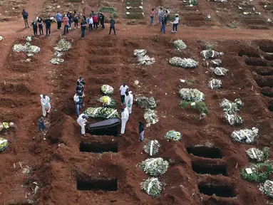 Petugas dengan pakaian pelindung menurunkan peti mati seseorang yang meninggal karena komplikasi COVID-19 ke dalam kuburan di pemakaman Vila Formosa di Sao Paulo, Brasil, Rabu (7/4/2021). Sao Paulo pada Rabu mulai menggali 600 kuburan tambahan setiap hari di pemakaman kotanya (AP Photo/Andre Penner)