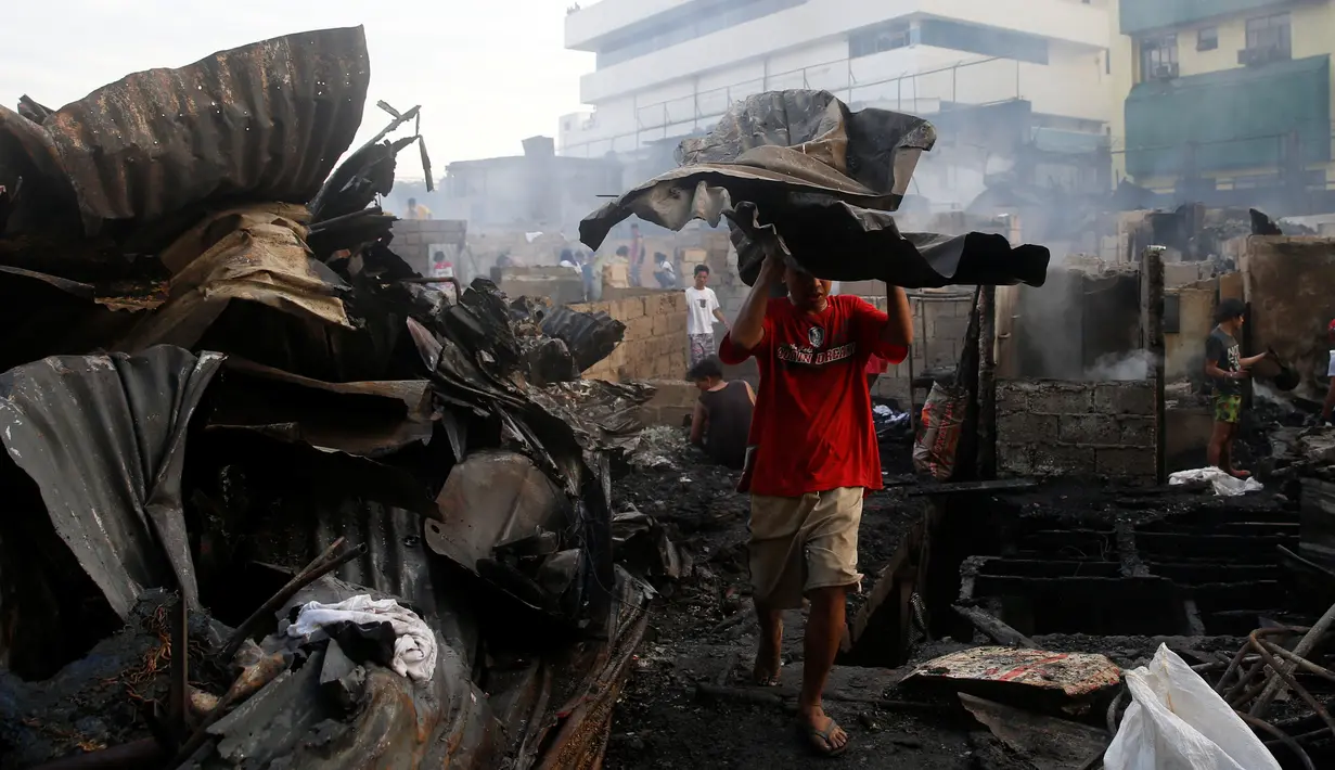 Seorang warga mengangkat puing-puing bangunan usai kebakaran kota Quezon, Metro Manila di Filipina (28/12). Dalam kejadian ini sejumlah warga mengalami luka-luka dan tidak ada korban jiwa. (REUTERS/Erik De Castro)