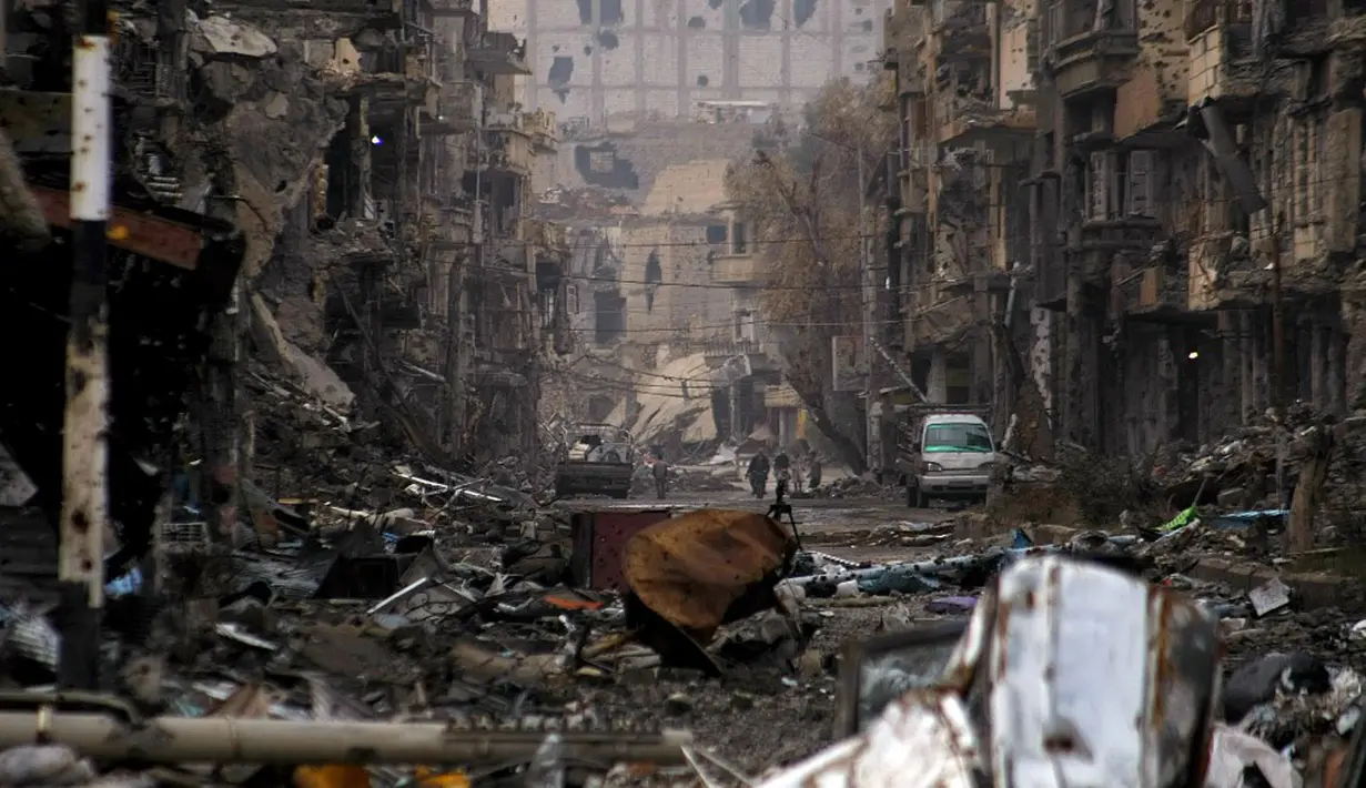 Warga berjalan di sepanjang jalan yang rusak parah di timur laut Kota Deir Ezzor, Suriah, 4 Januari 2014. (Photo by AHMAD ABOUD/AFP)